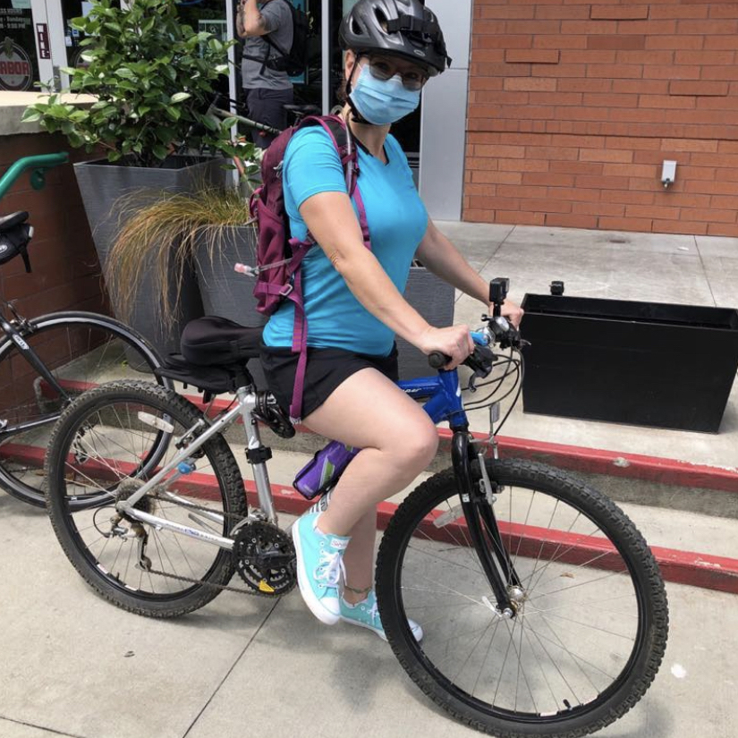 Shannon Lunch wearing a blue shirt and black shorts and blue Savvy converses and a face mask riding a bike