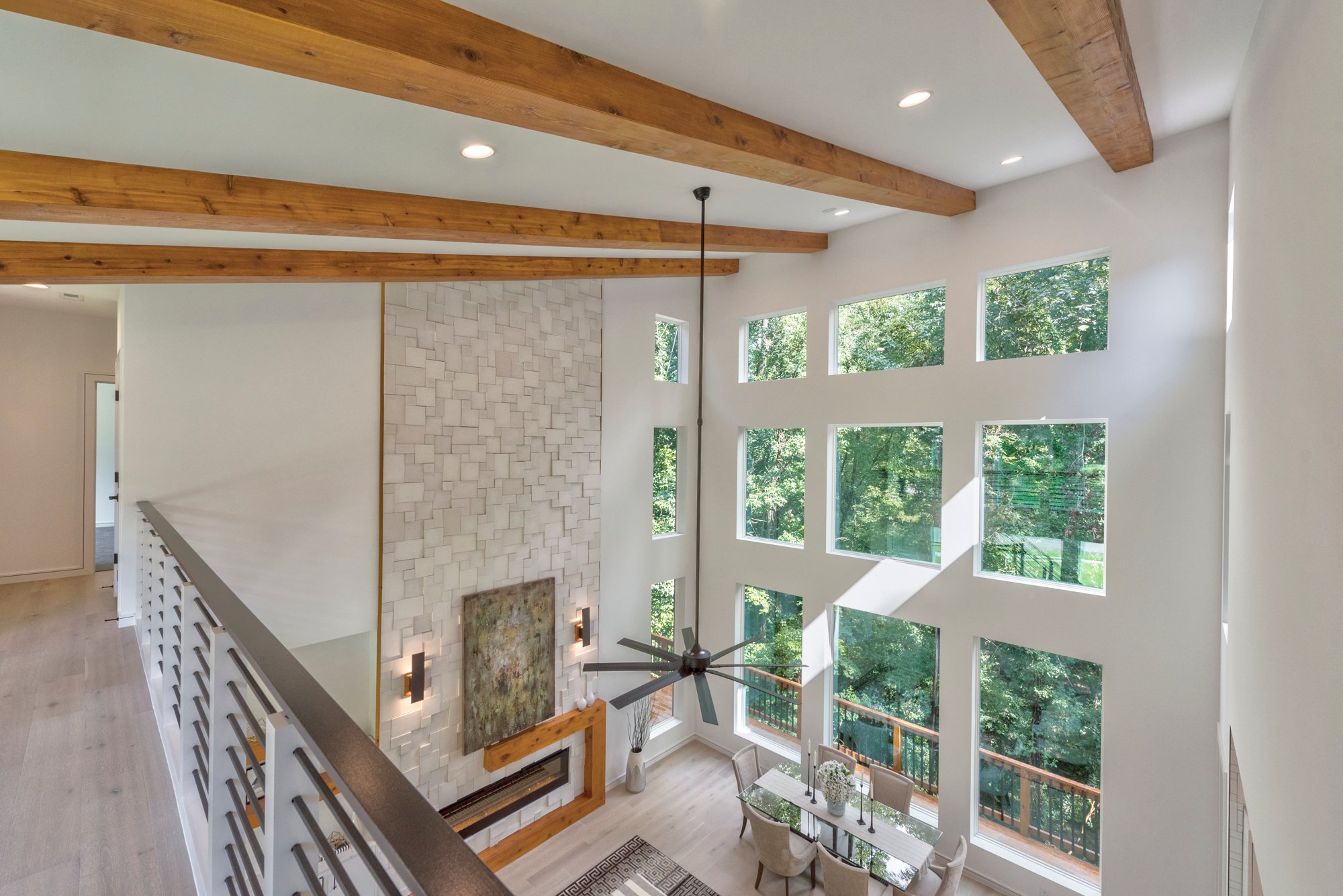 Second floor landing overlooking dining room with light wood floors and white walls with floor to ceiling windows and recessed lighting