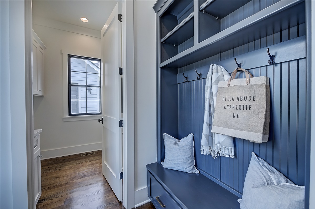 Mudroom with built in blue bench and cubbies with black hooks and white walls with black hinges and doorknob on door with black framed window and wood floors