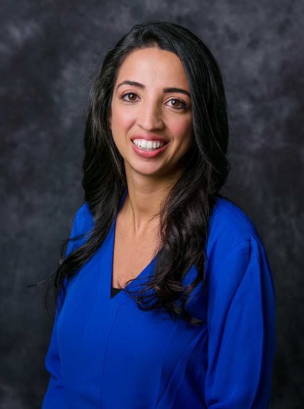 Lara Bucci wearing a long sleeve blue blouse standing in front of a gray backdrop