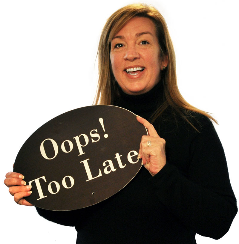 DanaPBurleson Dana P Burleson wearing a black turtleneck and holding a brown Oops! Too Late sign bubble standing in front of a white backdrop